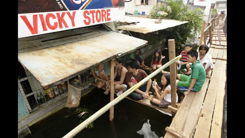 Filipinos rest on a footbridge above the flooded road.