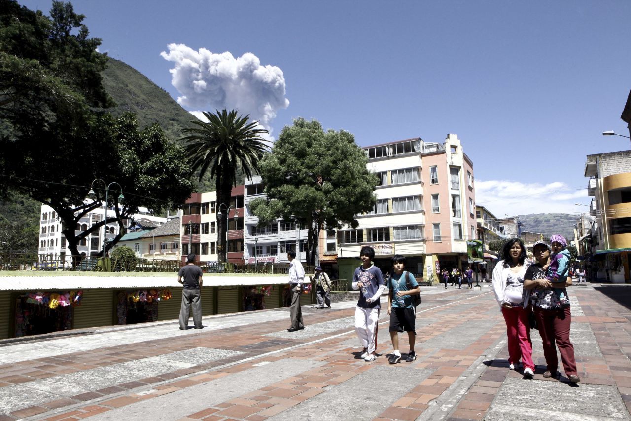Banos residents walk through the main square of town Tuesday as the nearby Tungurahua volcano spews ashes.