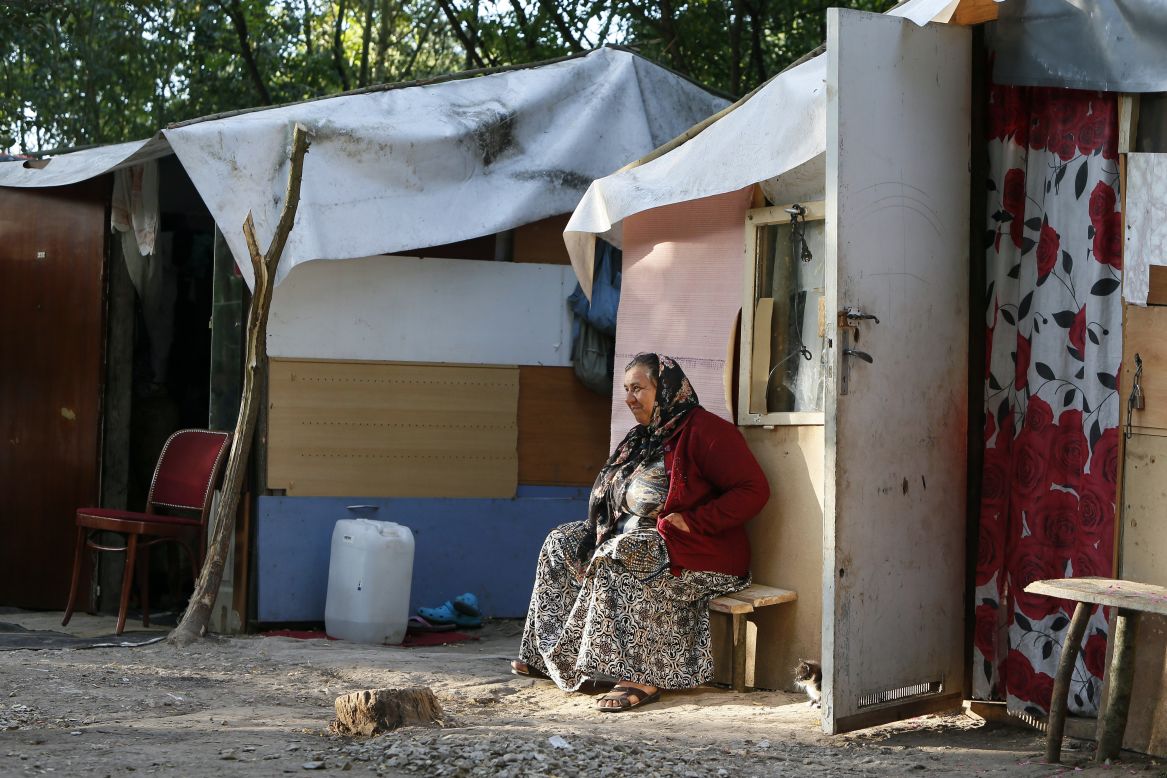 A woman from the Roma community sits in front of a shack.