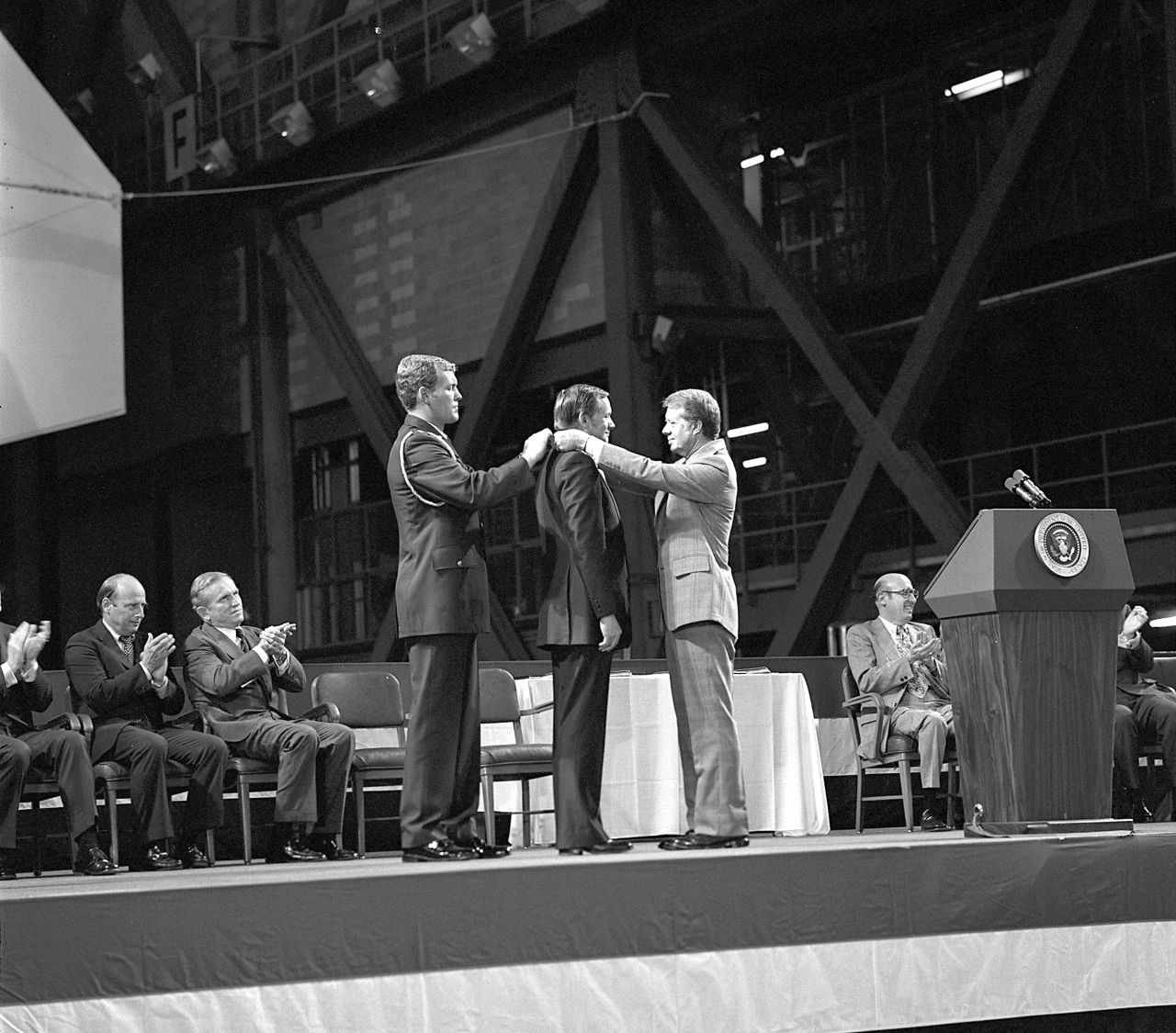 Armstrong receives the first Congressional Space Medal of Honor from President Jimmy Carter, right, assisted by Capt. Robert Peterson, on October 1, 1978. Armstrong, one of six astronauts to be presented the medal during ceremonies held in the Vehicle Assembly Building (VAB), was awarded for his performance during the Gemini 8 mission and the Apollo 11 mission.