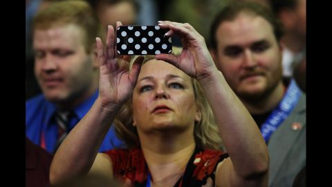 A woman captures the goings-on with her phone before the start of the shortened first day of the Republican National Convention.