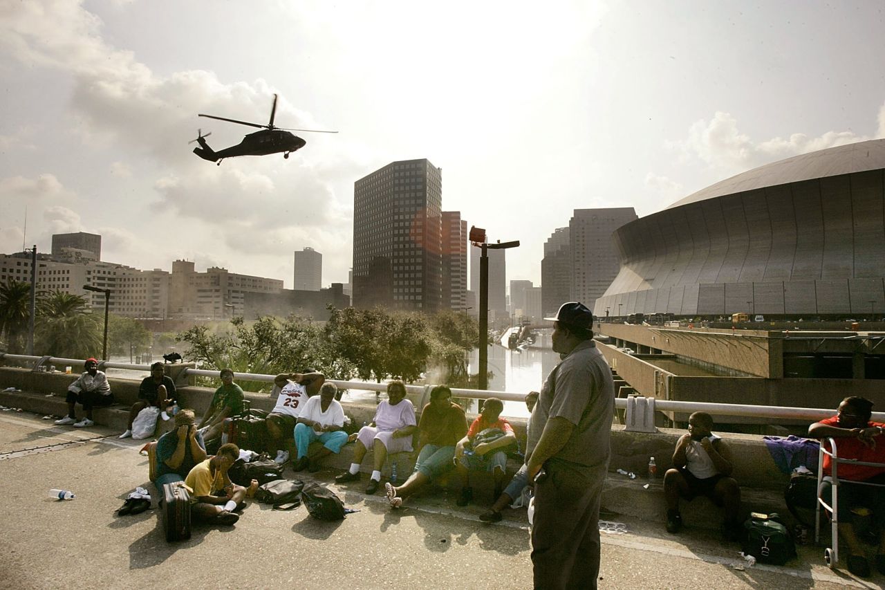People seek high ground on Interstate 90 as a helicopter prepares to land at the Superdome in New Orleans on August 31, 2005.