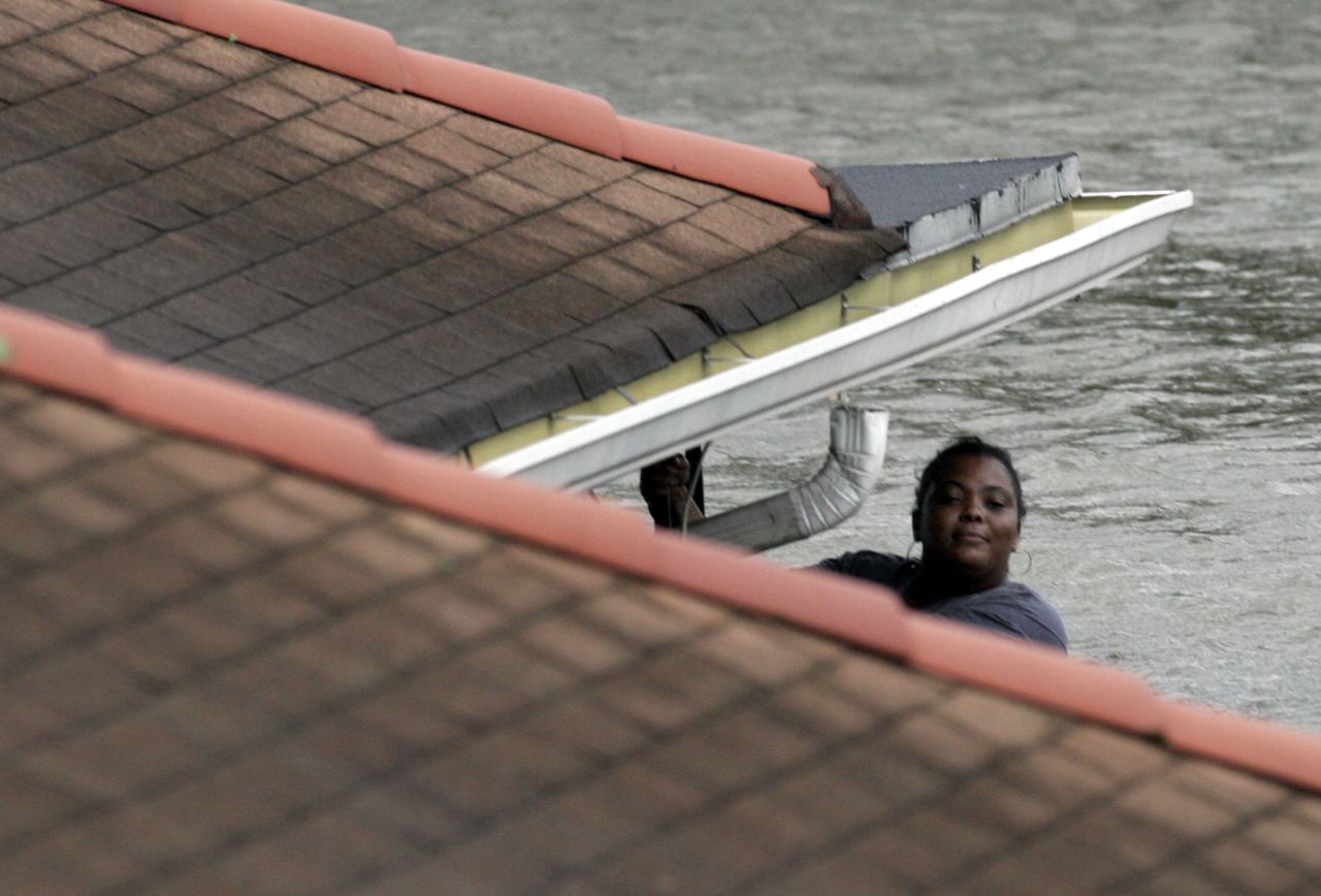 Hanging from her roof, a woman waits to be rescued by New Orleans Fire Department workers on August 29, 2005.