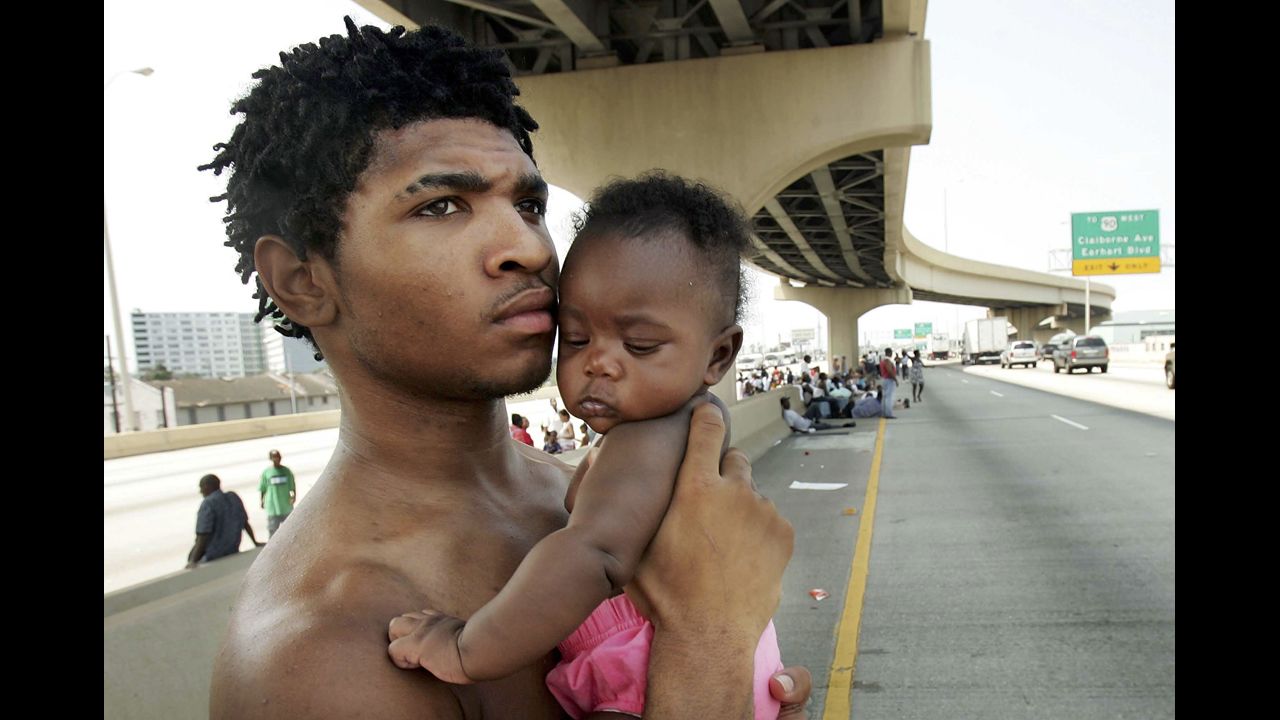 Daryl Thompson and his daughter Dejanae, 3 months old, wait with other displaced residents on a highway to catch a ride out of New Orleans on August 31, 2005. Thousands were looking for a place to go after leaving the Superdome shelter.