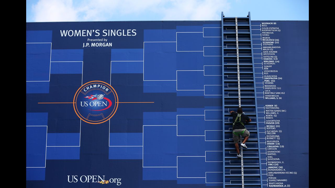 A worker climbs a ladder to adjust the board displaying the women's draw.