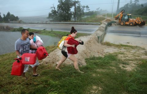 Residents carry pillows, blankets and fuel containers past a flood berm while evacuating an area of rising floodwaters on Thursday in Slidell.