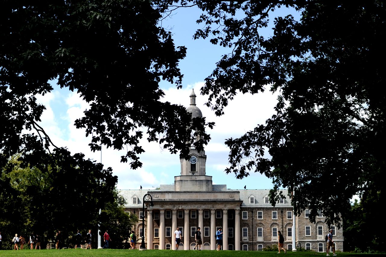 The clock tower of the Old Main building peeks through the trees on campus.