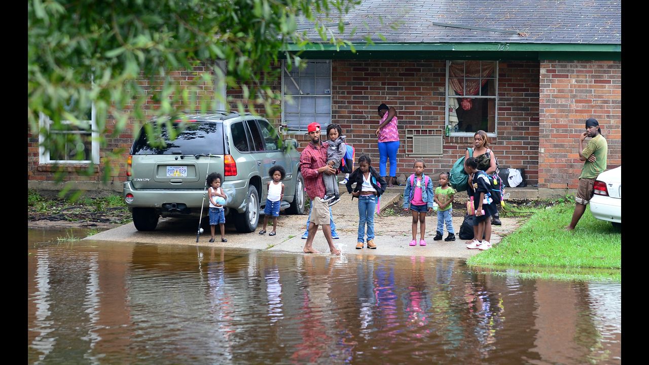 Residents stand in front of their home as flooded streets engulf their neighborhood in Slidell.
