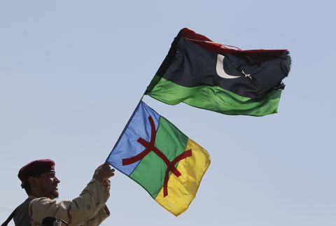 A soldier waves Libyan and Amazigh flags on the frontline of battle against the remnants of the Gadhafi regime in September 2011. The red symbol on the Amazigh flag is the character for "free man," the name by which Berbers to themselves in Tamazight.