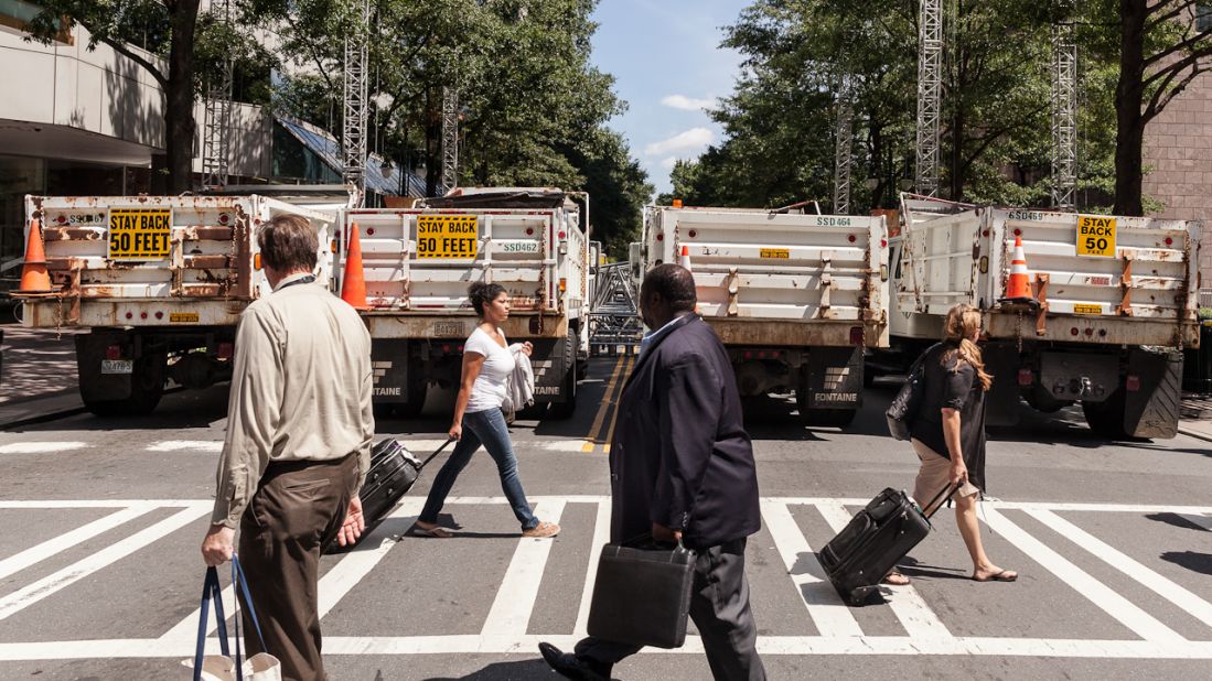 Pedestrians walk past dump trucks Sunday that are serving as barriers.