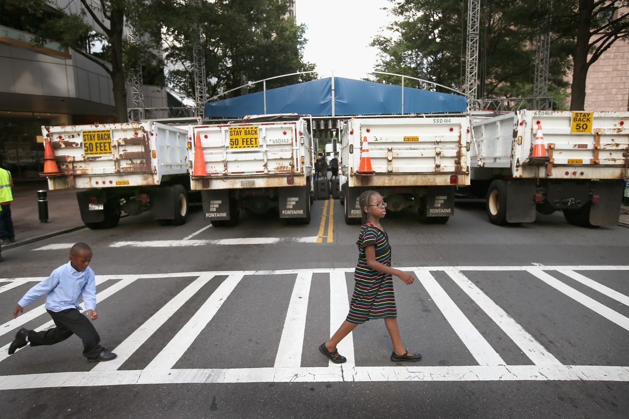 Children cross the street in front of a row of dump trucks used as a barricade near the Bank of America headquarters in downtown Charlotte on Sunday. 