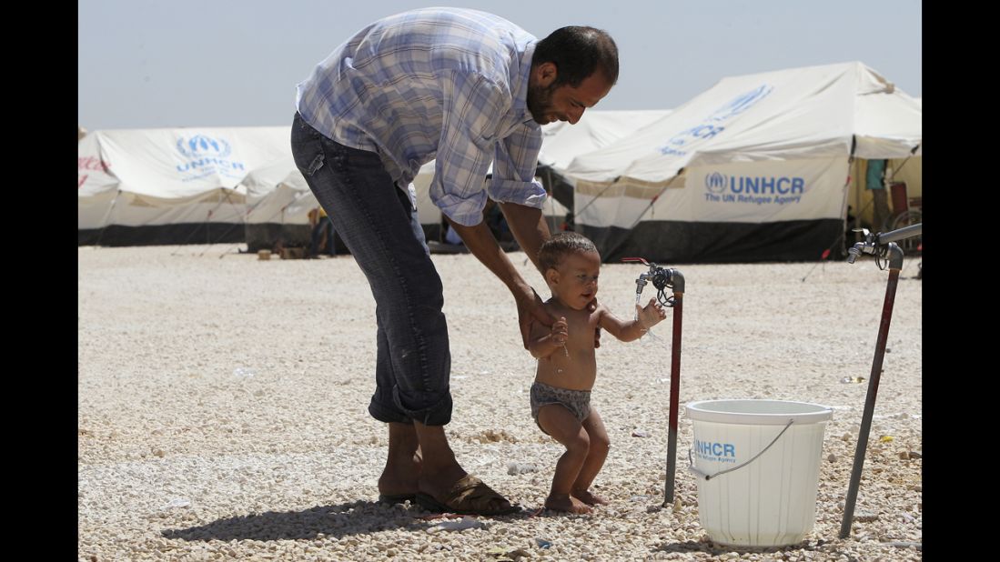 A Syrian refugee bathes his child. Water is provided several times daily by water trucks, but supplies of fresh water are very limited and the needs of the refugees are putting pressure on local communities which already experience water shortages.