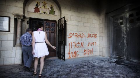 Tourists look at a burnt door as they walk past grafitti sprayed on the wall of the Christian Catholic Latrun monastery on Tuesday.