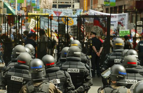 <strong>2004: </strong>Riot police stand ready inside the gates of Boston's FleetCenter, site of the Democratic National Convention, as protesters march past.  