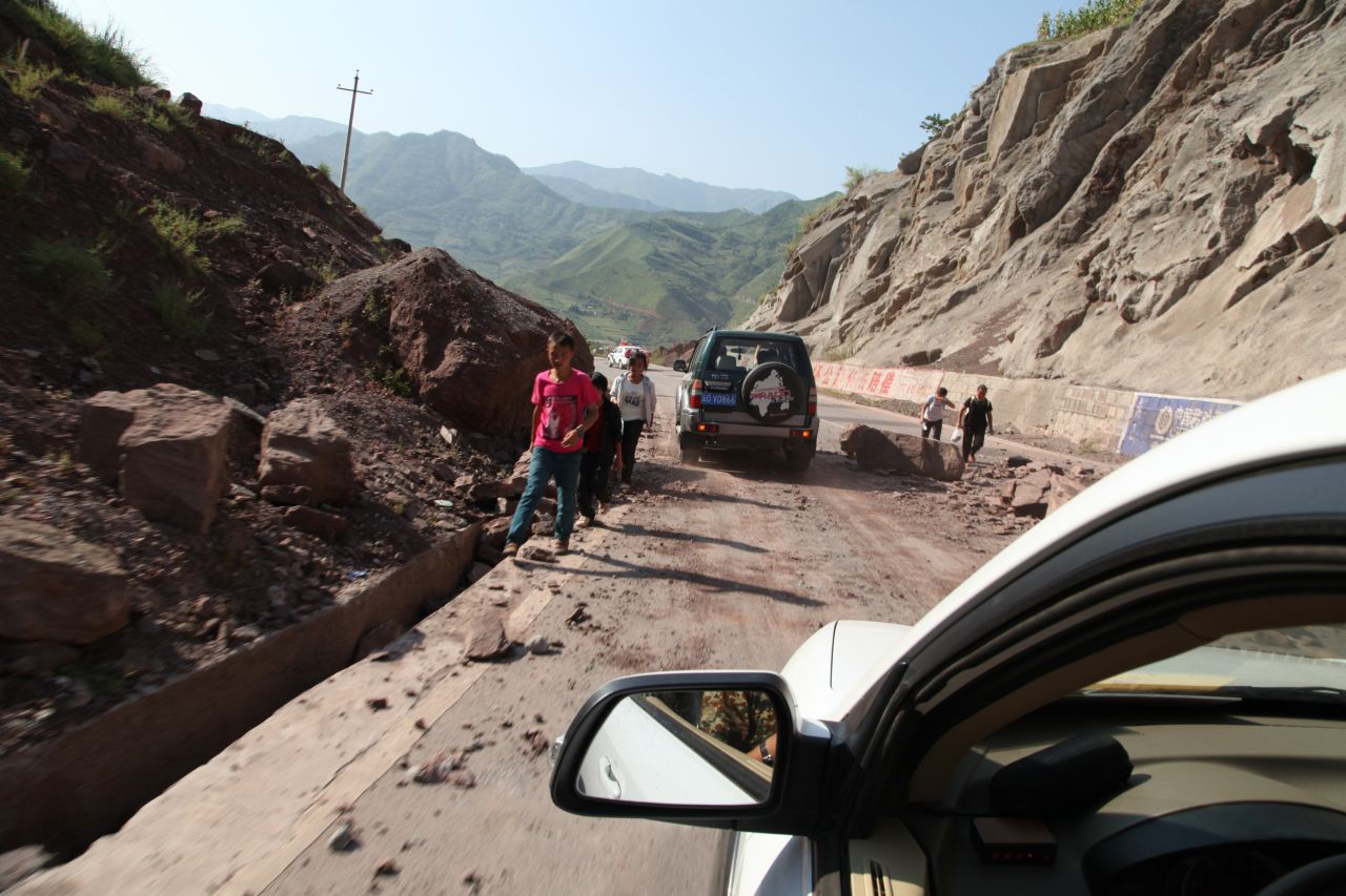 Vehicles make their way slowly along the road after rocks tumbled in Yiliang.