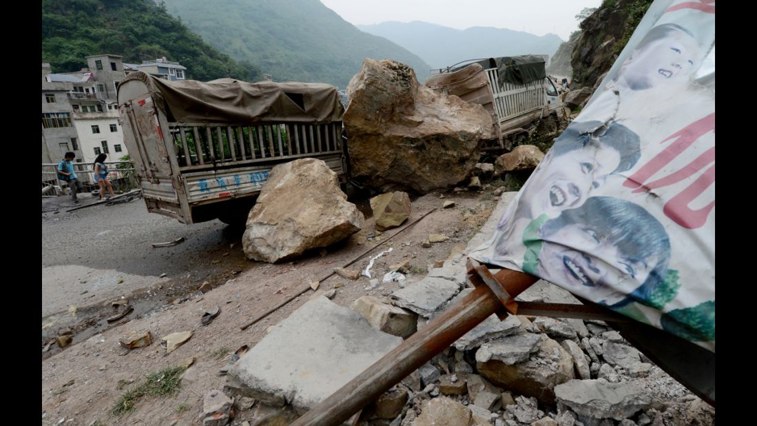 Local residents walk past destroyed vehicles at a landslide area on Saturday. 