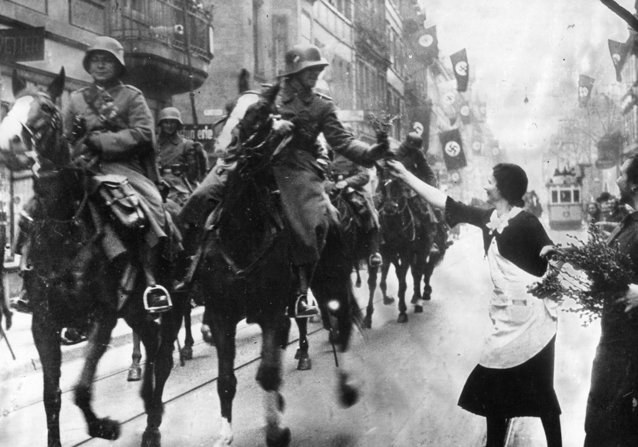 German Nazi leader Adolf Hitler violates the Locarno Pact and the Treaty of Versailles on March 7, 1936, by sending German forces, seen here receiving flowers by well-wishers, to the demilitarized Rhineland.