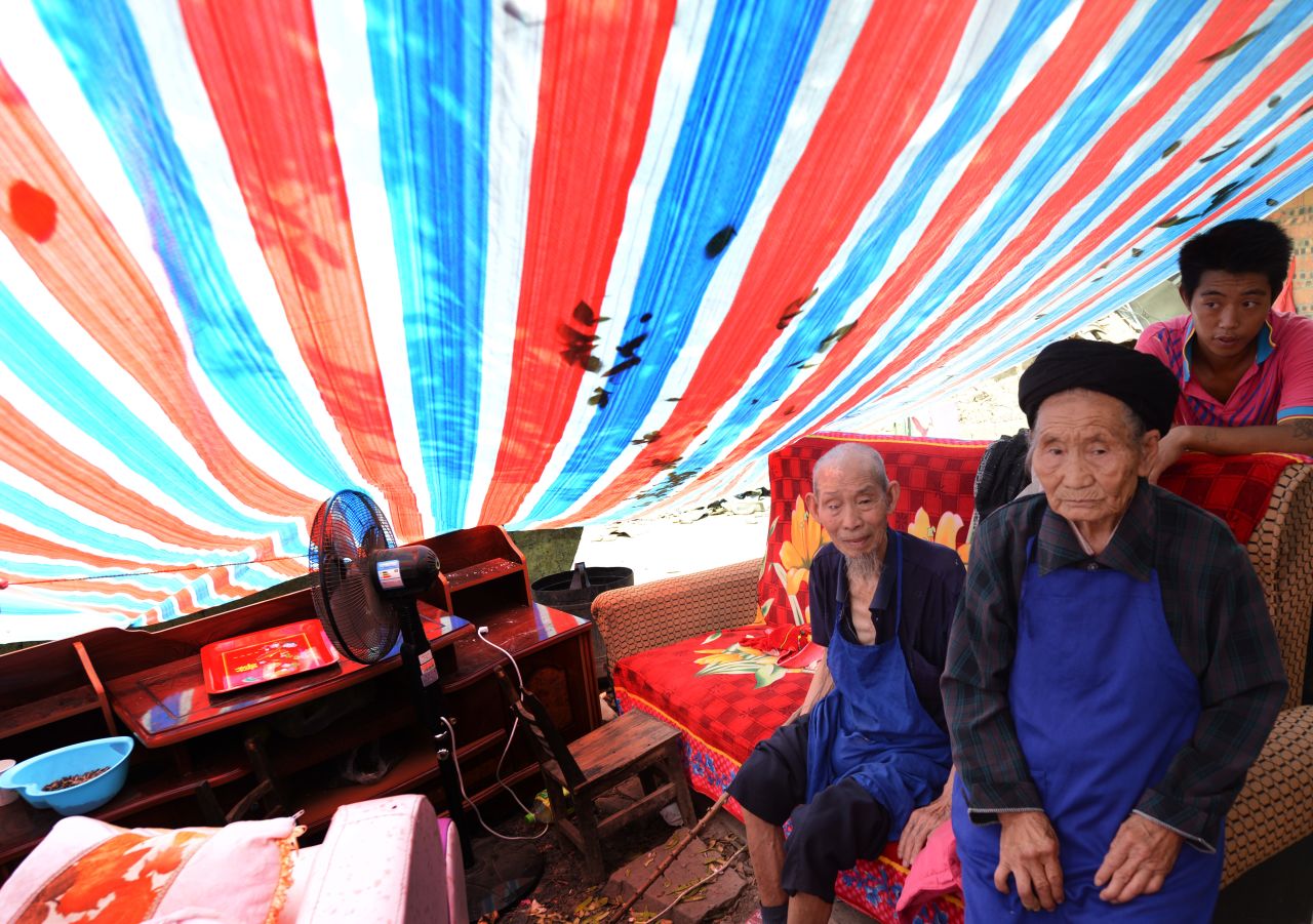 Elderly members of the Peng family sit in their makeshift shelter on Monday after their home was badly damaged.