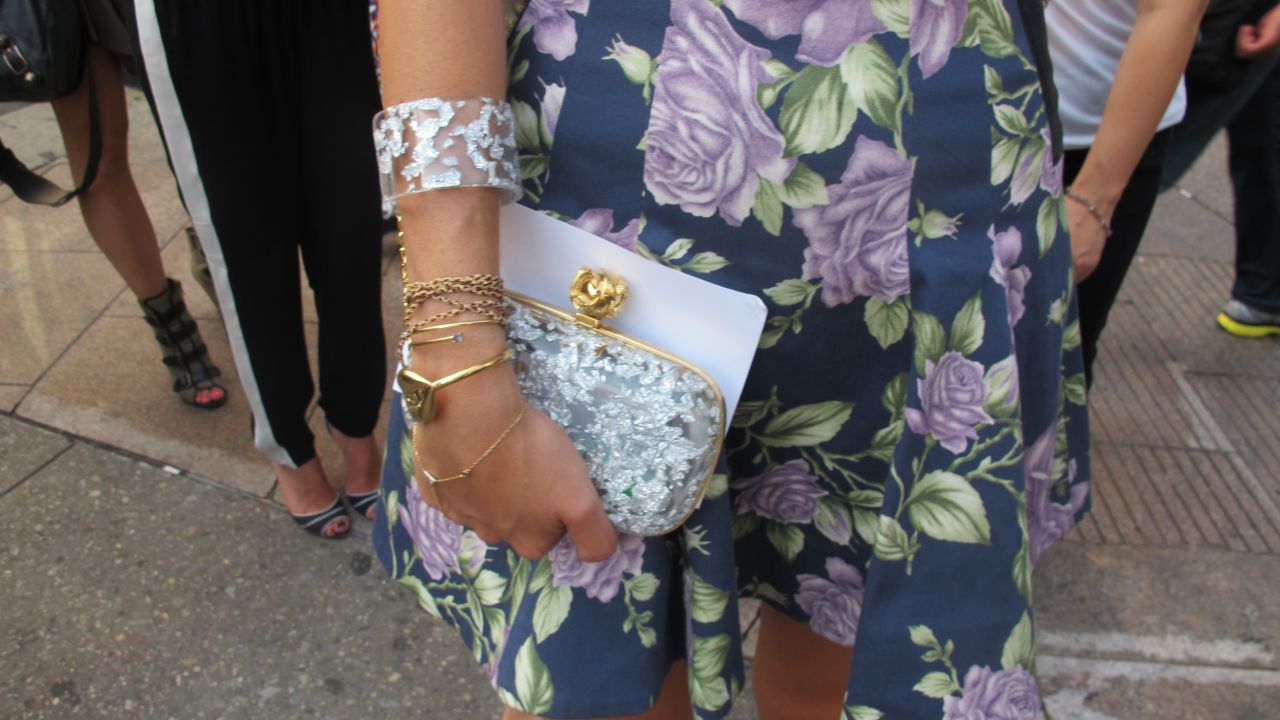 Medine carries a hard shell clutch by Reece Hudson with a chain linking it to a bracelet.