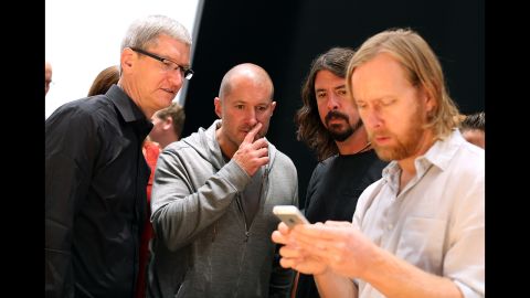 Apple CEO Tim Cook, left; Jonathan Ive, senior vice president of industrial design; and Dave Grohl of the Foo Fighters watch Foo Figters' bassist, Nate Mendel, handle the iPhone 5.
