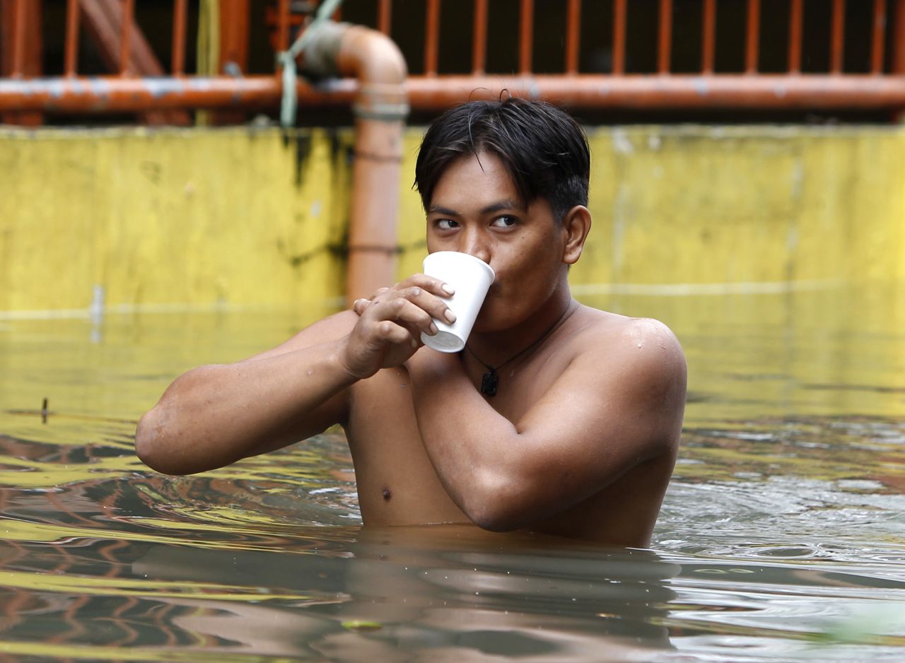 A man drinks a cup of coffee as he wades through water in San Juan on Saturday.