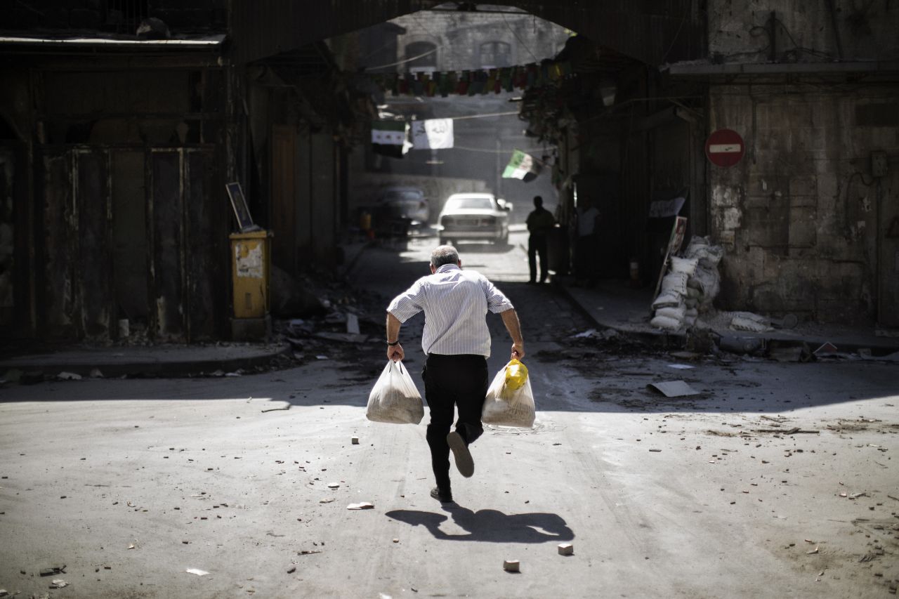 A Syrian man carrying grocery bags tries to dodge sniper fire as he runs through an alley near a checkpoint manned by the Free Syria Army in Aleppo on September 14.