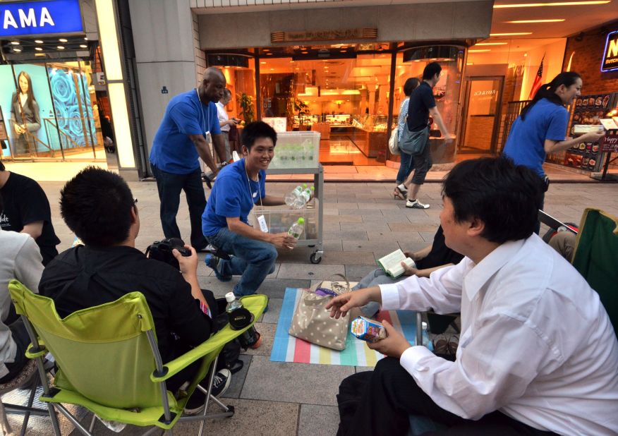 Apple store staff hand out free drinks and chocolate to Apple fans queuing on the sidewalk for the launch of Apple's new iPhone 5 in Tokyo.