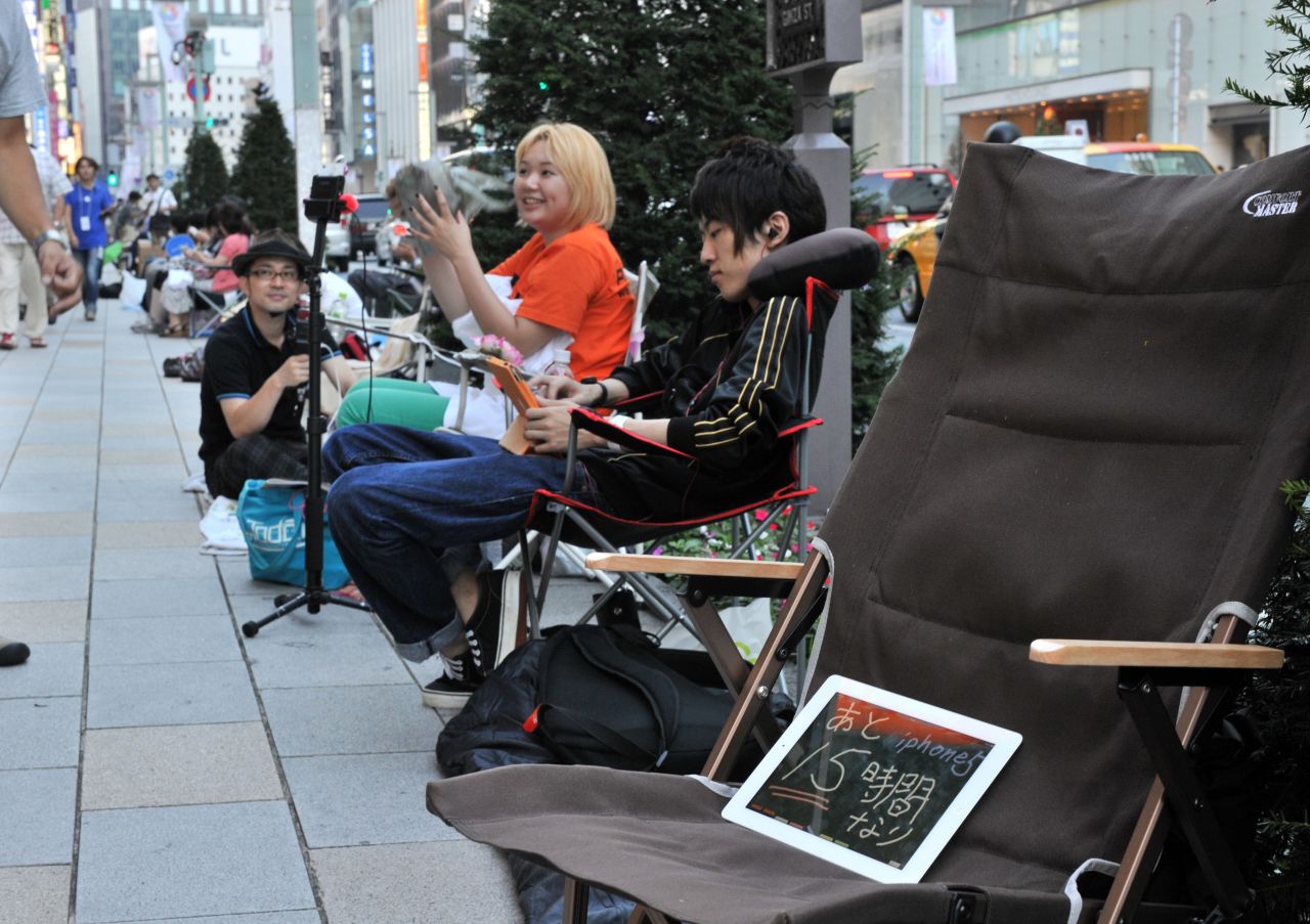 Apple fans line up outside an Apple Store in Tokyo on Thursday. The iPad in the chair reads "15 hours more for iPhone 5."