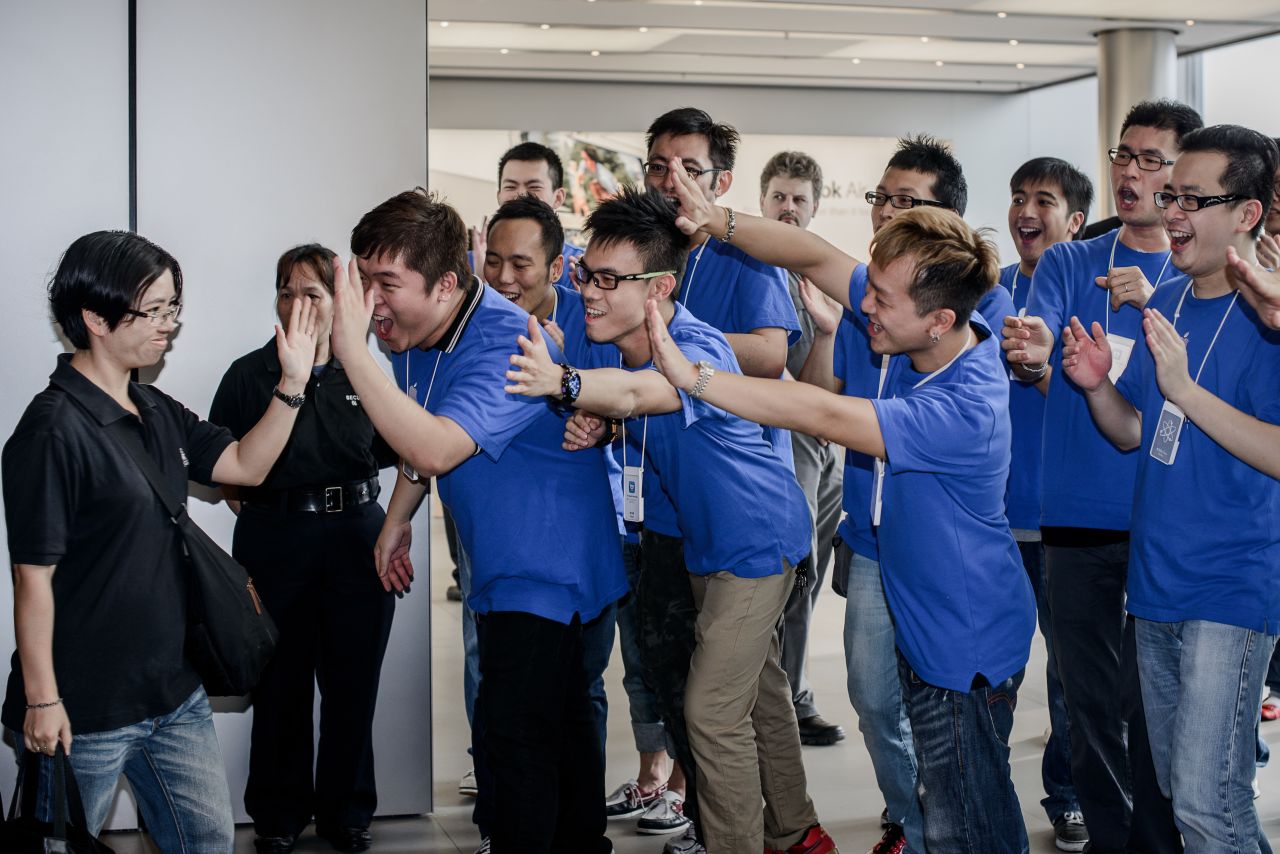 A customer, left, is greeted by employees as she enters the Hong Kong Apple store.