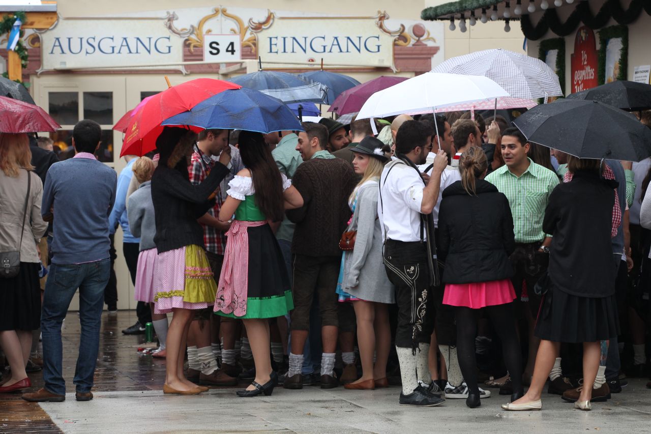 Visitors hold umbrellas as they wait in front of a beer tent.