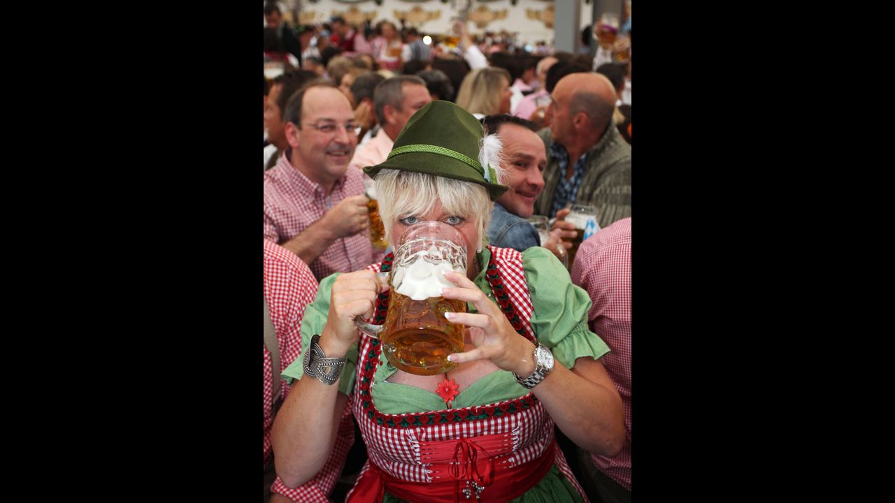 A woman wearing a traditional Bavarian Dirndl dress drinks beer.