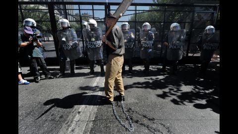 An elderly man with his legs chained stands in front of riot police protecting the Greek parliament Wednesday.