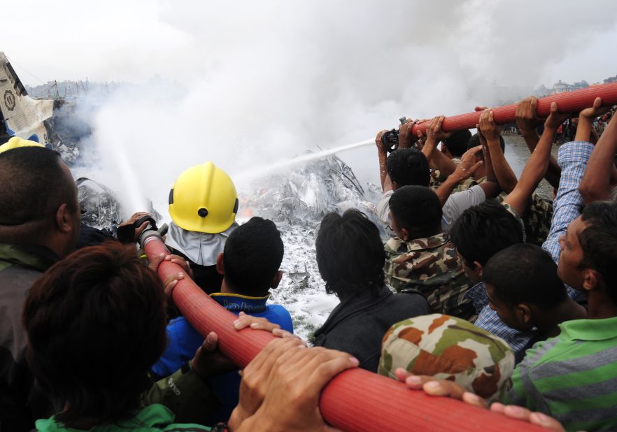 Nepalese firefighters and volunteers try to put out flames from the wreckage.