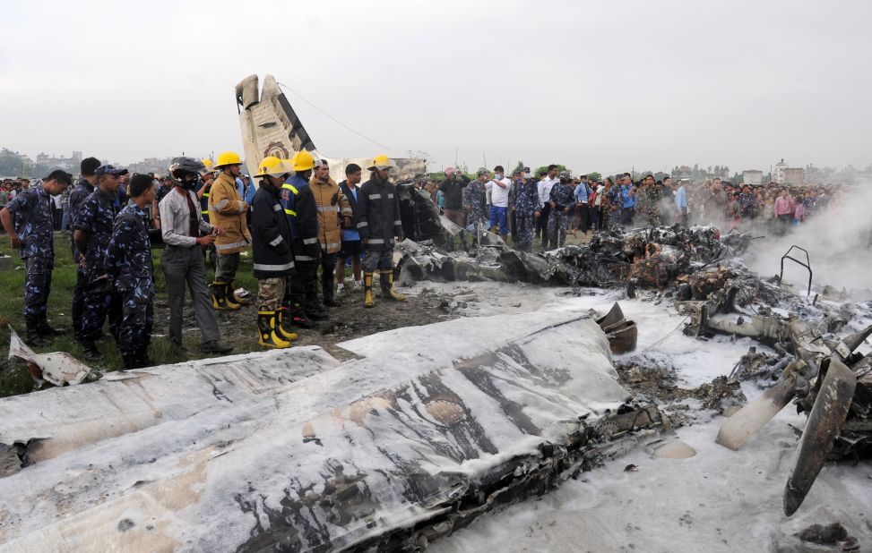 Firefighters and volunteers stand near the wreckage. The plane crashed on the banks of the Manohara River in Bhaktapur District, Nepal's Civil Aviation Authority said.