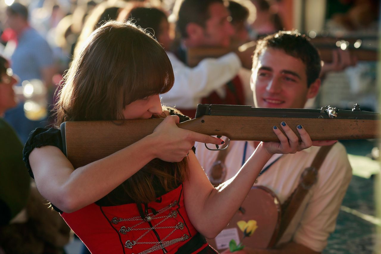 A girl wearing a Bavarian Dirndl dress fires a rifle at a shooting range at Oktoberfest.