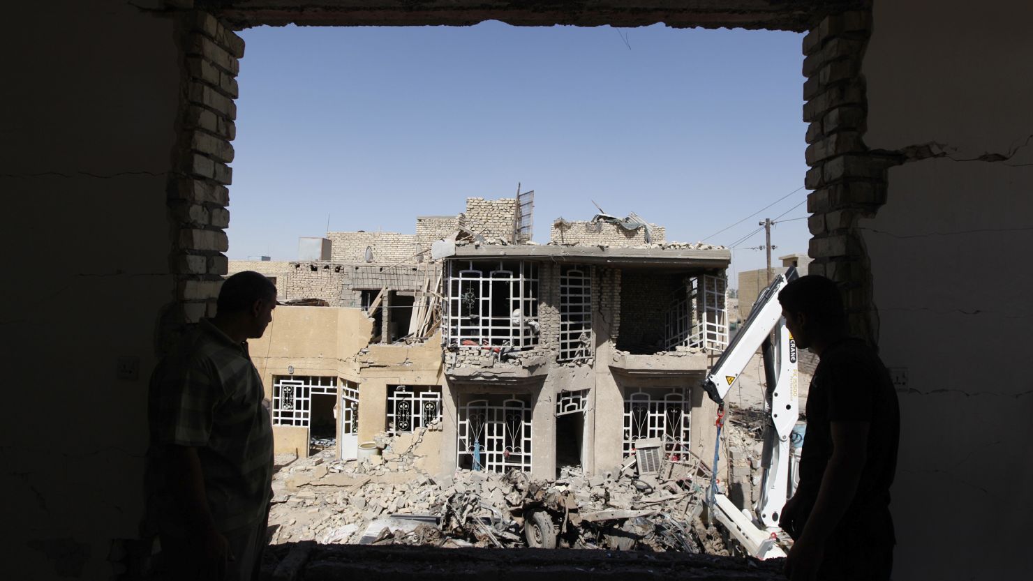 Residents look on as they stand at the site of a bomb blast in the town of Taji, north of Baghdad, Sunday.