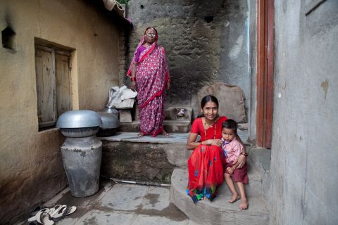 Sai, who is almost three years old, sits with mother and neighbor outside her home. Anganwadi workers counsel her mother about how, when and what to feed Sai to increase her weight.