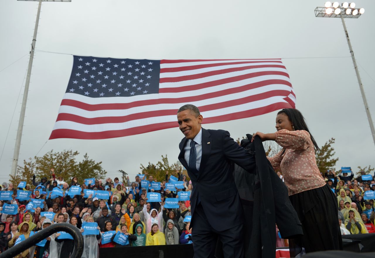 Obama is assisted with putting on a raincoat onstage during a campaign rally at Cleveland State University on Friday.
