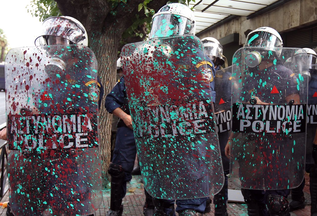 Riot police are covered with paint thrown by protesters.