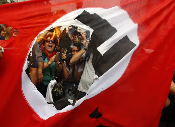 Demonstrators burn a Nazi flag during a demonstration against the visit of German Chancellor Angela Merkel in Athens on Tuesday, October 9. Merkel arrived in Greece on her first visit since Europe's debt crisis erupted three years ago, and protesters geared up to show their discontent with European Union-imposed austerity measures. <a href="index.php?page=&url=http%3A%2F%2Fwww.cnn.com%2FSPECIALS%2Fworld%2Fphotography%2Findex.html" target="_blank">See more of CNN's best photography</a>.