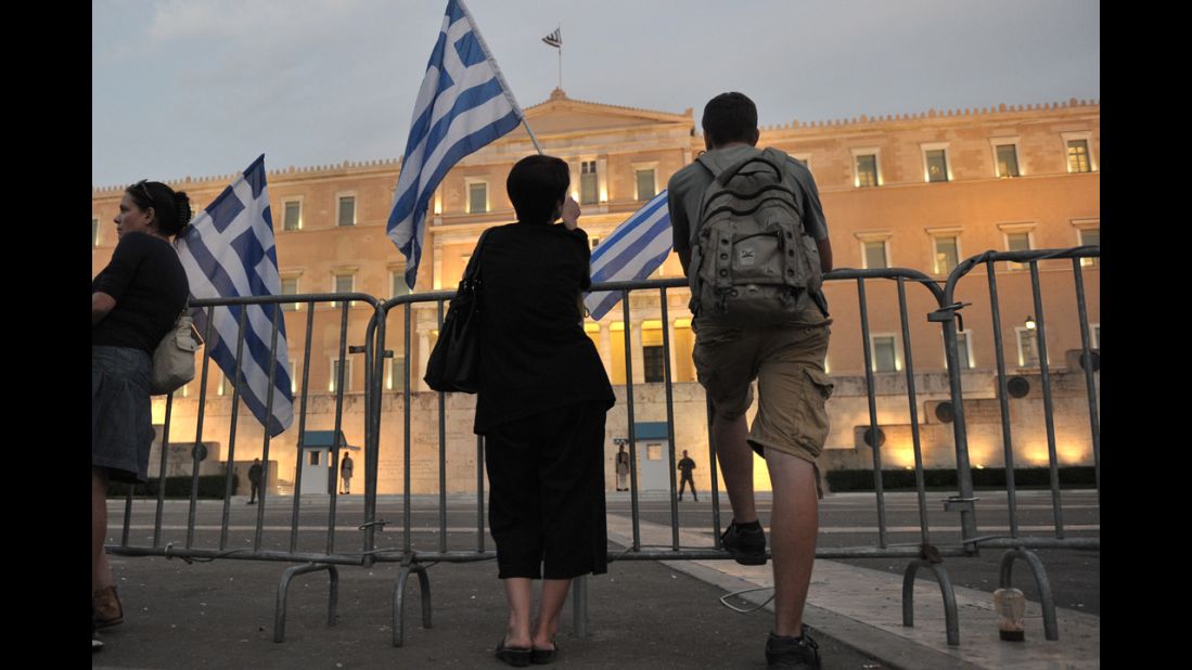 Protesters hold Greek flags behind barriers in front of the Greek Parliament.