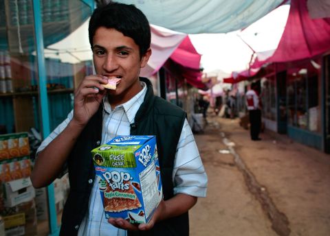 An Afghan merchant takes a bite of a Pop-Tart outside at the Bush Market on October 29, 2006 in Kabul, Afghanistan. The small black market named after ex-U.S. President George W. Bush is flooded with cheap American goods coming from military surplus, as well as some stolen goods.