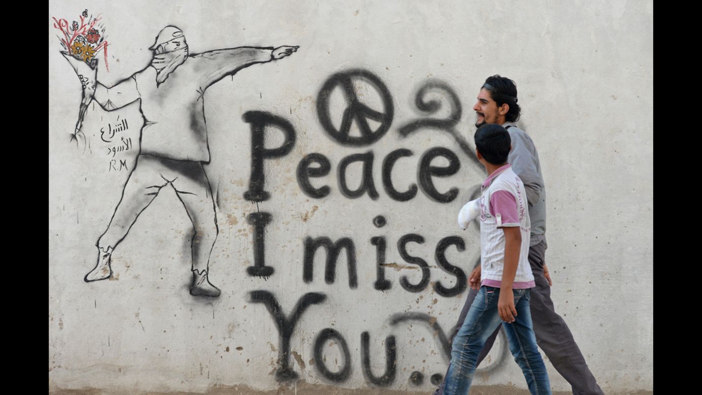 Syrian youths walk past graffiti in the rebel-held city of Minbej on Wednesday.