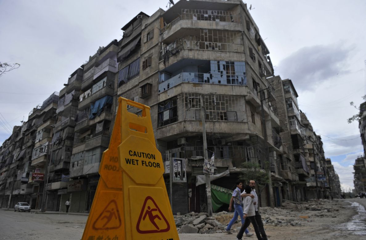 Syrian civilians walk in front of damaged buildings in Aleppo on Thursday.