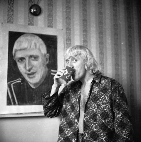 The first presenter of long-running music program "Top of the Pops," Savile poses by a portrait of himself in February 1965, while enjoying his regular breakfast of Coke and a cigar in a central London hotel room.