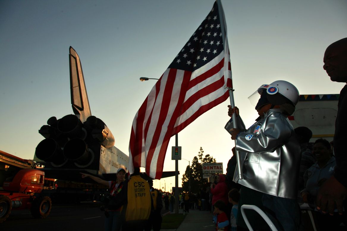 Amir Morris, 3, wears an astronaut costume while holding an American flag as the space shuttle crawls past.