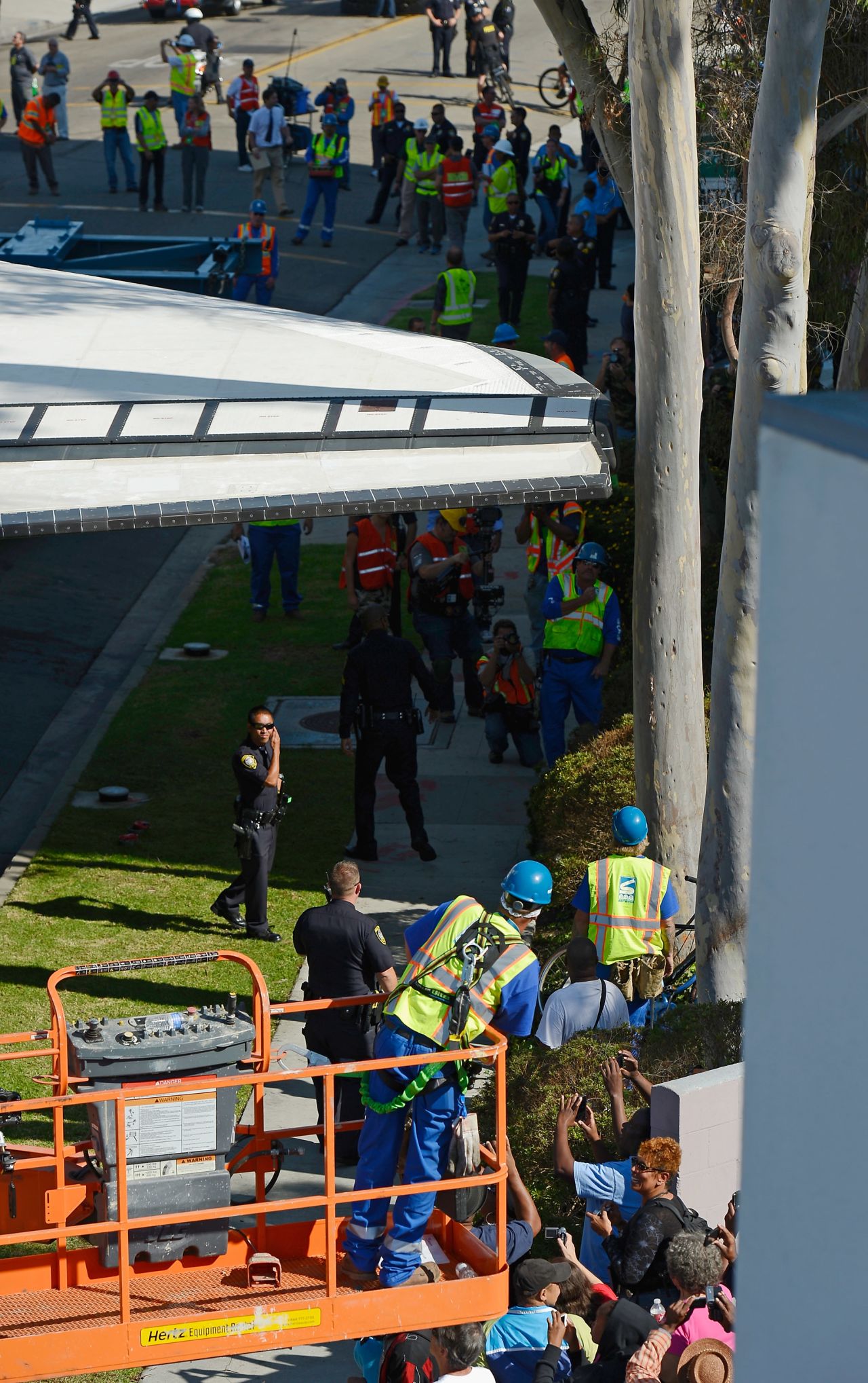 Workers and officials look on as Endeavour squeezes past a tree.