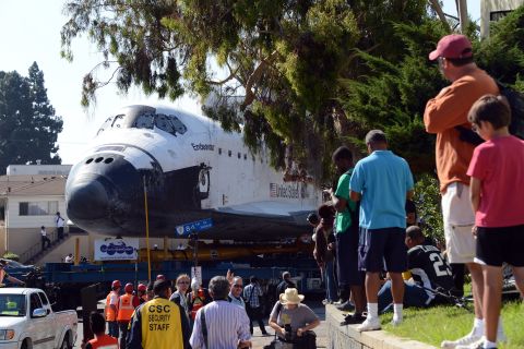 People watch as the shuttle makes its way up a narrow street.