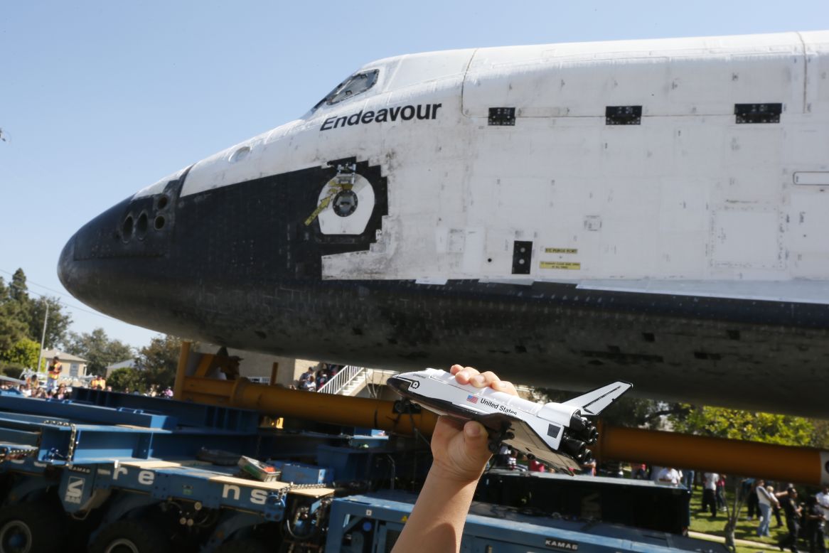 A boy holds a model of  Endeavour as the real thing rolls past.