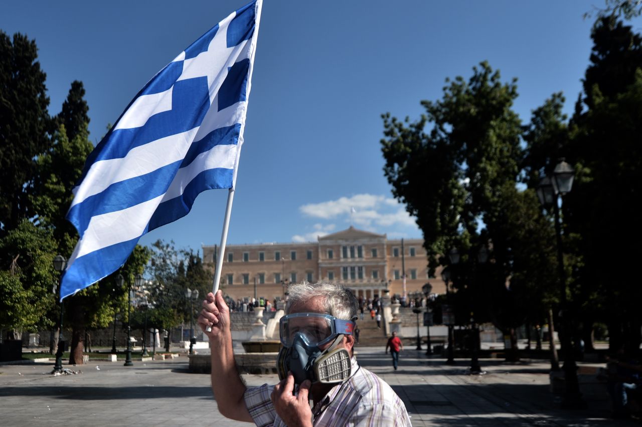 A demonstrator wearing a gas mask waves a Greek flag during clashes between police and anti-austerity protestors in Athens. Police fired tear gas to disperse demonstrators after they broke through a police line outside luxury hotels on central Syntagma Square.